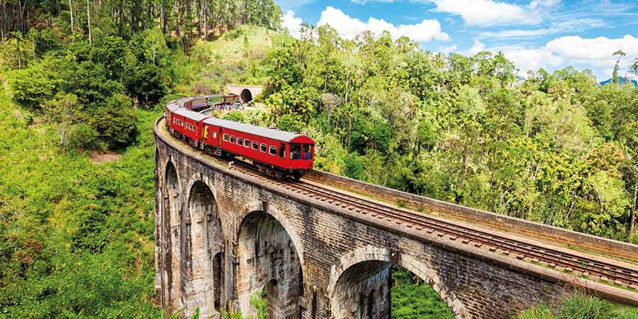 A red train passes over the Nine Arches Bridge.